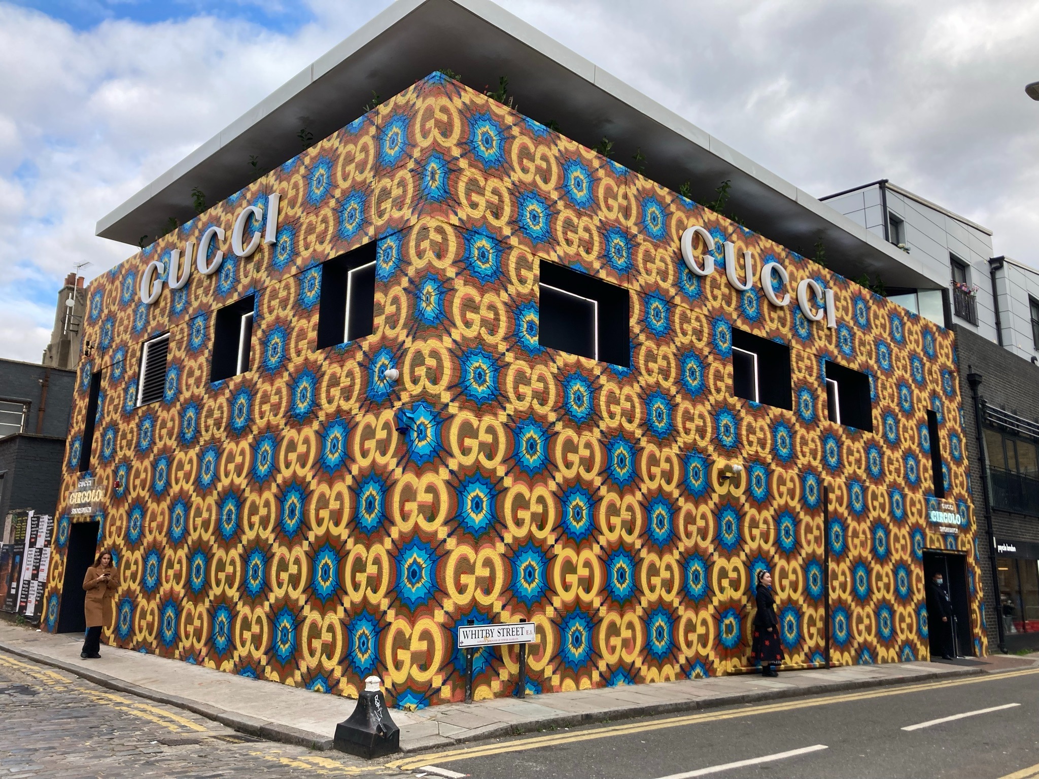 Vue d’angle des deux façades du Gucci Circolo Shoreditch à Londres, couvertes de motifs GG colorés et d’enseignes GUCCI.